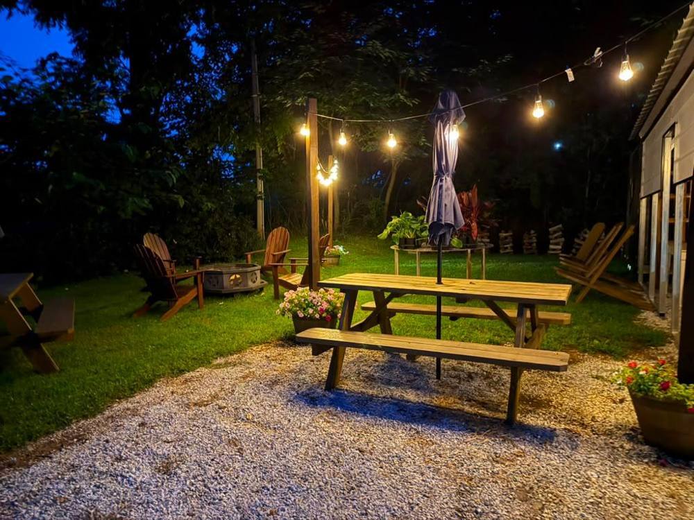 String lights glowing over picnic tables and a fire pit at night